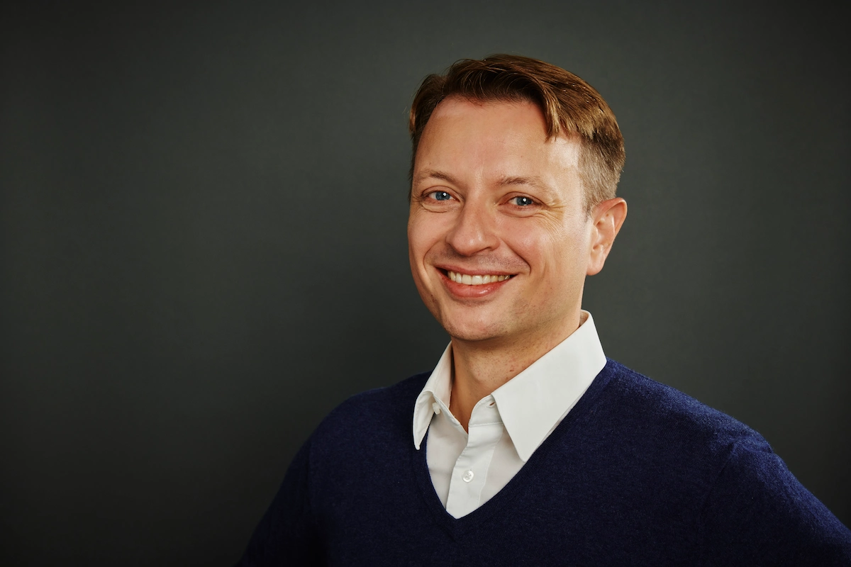 Profile photo of Christian Baumgertel smiling against a dark grey backdrop.